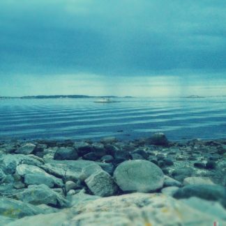 Türkisblaues, sehr körniges, etwas unscharfes Bild, das sanfte Meereswellen hinter steinigem Strand zeigt. In Bildmitte ein schemenhaftes Schiff.
