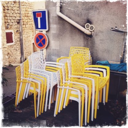 Gelbe und weiße Plastikstühle stapeln sich vor einem Sackgassen-Schild in einer verwinkelten französischen Ortschaft