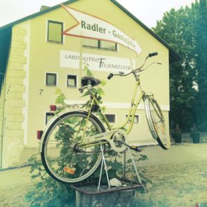 Ein Dreigang-Damenrad aufgebockt auf einem Sockel vor einem Haus mit großem Schriftzug Radlergaststätte