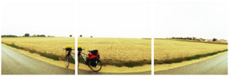 Vor einem abgeernteten Getreidefeld steht ein bepacktes Reiserad. Die Gegend ist flach bis zum Horizont.