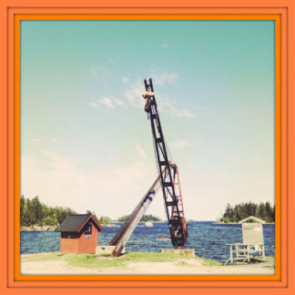 An einem Hafen in den Ostsee-Schären. Ein Kran ragt hoch in den blauen Himmel. Dashinter Meer, Wald, eine kleine Hütte. Das Bild hat einen auffälligen orangenen dreifachen Rahmen.