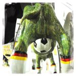 Blick underfoot auf den Hintern einer kunststoffenen Kuh. Das Euter ist ein Fußball. Sie trägt Socken mit Deutschlandfarebnbund. Ihr Körper ist grün.