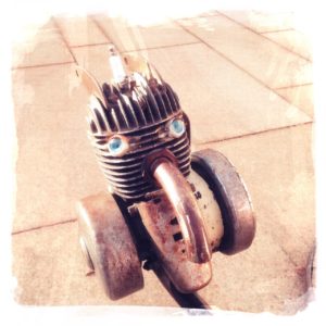 Ein Einzylindermotor auf blassbeigem Pflaster mit Rädern, der aussieht wie ein Kopf.