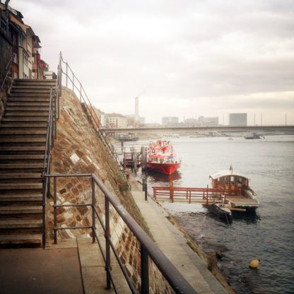 Links im Bild eine Treppe, die zum Ufer führt, an dem ein paar Boote verankert sind.