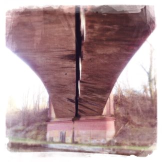 Unter einer braunen Eisenbahnbrücke erhascht man einen Blick auf den Fluss, das Ufergewächs und die Brückenkonstruktion. Durch Verfremdung wirkt das Foto wie ein Gemälde.