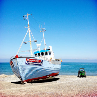 Links im Bild ein hellblaues Boot mit roter Zierfarbe auf dem Strand. Rechts daneben ein winzig anmutender alter Traktor.