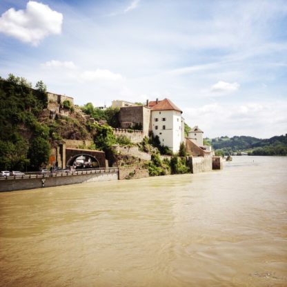 Blick über die Donau auf ein stattliches Gebäude über einem Straßentunnel.