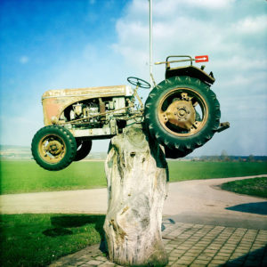 Auf einem Baumstumpf ist ein alter Traktor etwa anderthalb Meter hoch schwebend angebracht.