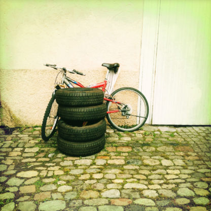 Ein Stapel abgefahrener Reifen, vier Stück vor einem Fahrrad, das an einer Hauswand lehnt.