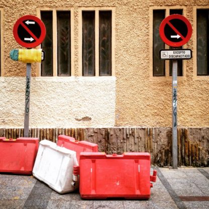 Zwei Parkverbotsschilder rechts und links im Bild vor einer Hauswand. Spanische Aufschrift. Dazu einige weiße und rote mobile Barrieren als chaotisches Ensemble.