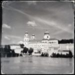 Über en Inn hinweg blickt man auf Passaus Dom mit drei gut sichtbaren Türmen mit runden Kuppeln. Das quadratische Schwarz-weiß-Bild ist im Retrostil mit auffransenden Rändern. Markant der Himmel unter Zirruswolken.