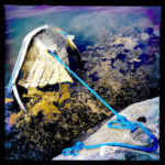 Ein gesunkenes Boot, dessen Bug aus dem Wasser steht liegt vertäut neben einem Felsen.