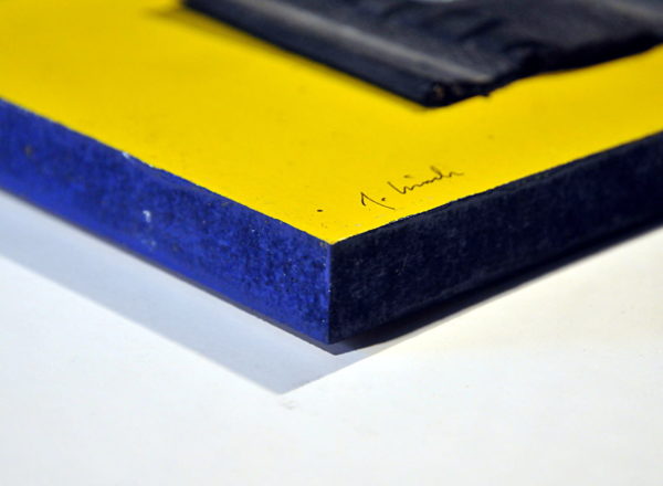 Auf einem gelben Bildträger ist ein Reifenstück, quadratisch mit derbem gesägten Rand aufgeschraubt mittels Linsenkopfschraube und Unterlagsscheibe mittig. Der fingerdicke Rand des Bildträgers ist blau bemalt
