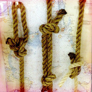 Drei Seemannnsknoten hängen vor einer blassen Seekarte als Dekoration auf einer Fähre.