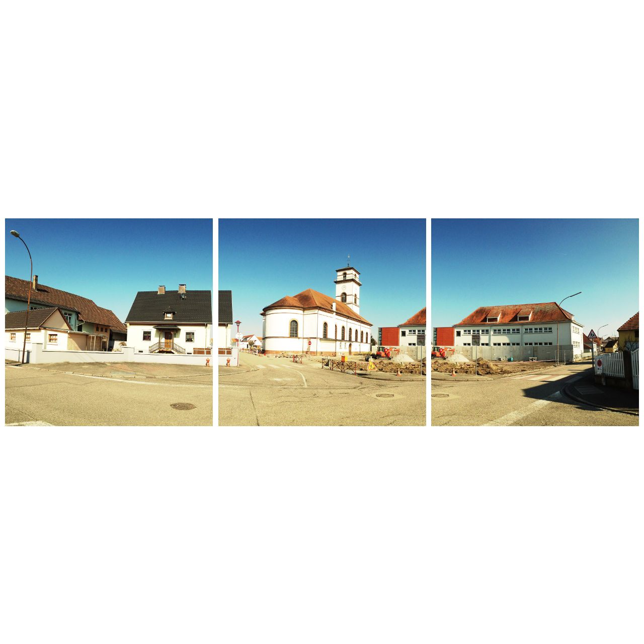 Zentrales Motiv als teil einer Dorfplatzszene in Drusenheim, Frankreich. Hinter einer Baustelle erhebt sich eine weiße Kirche mit rotem Dach. Die beiden Bilder rechts und links zeigen Wohngebäude mit Sattel- und Krüppelwalmdächern.