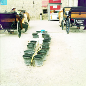 Zwischen zwei geparkten Salzburger Fiakernsteht eine Reihe Blecheimer bereit, um die Pferde zu tränken.
