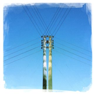 gespiegelter Strommast, dessen Kabel wie ein Spinnenetz über dem blauen Himmel liegen.