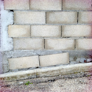Das monochrom graue Bild einer schräg und chaotisch gemauerten Wand aus Bimssteinen, Beton und Zement.