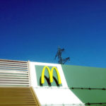 Aufnahme des Dachs eines Mac Donald's Ladens mit gelbemM. Im Hintergrund ragt ein Strommast in den tiefblauen Himmel