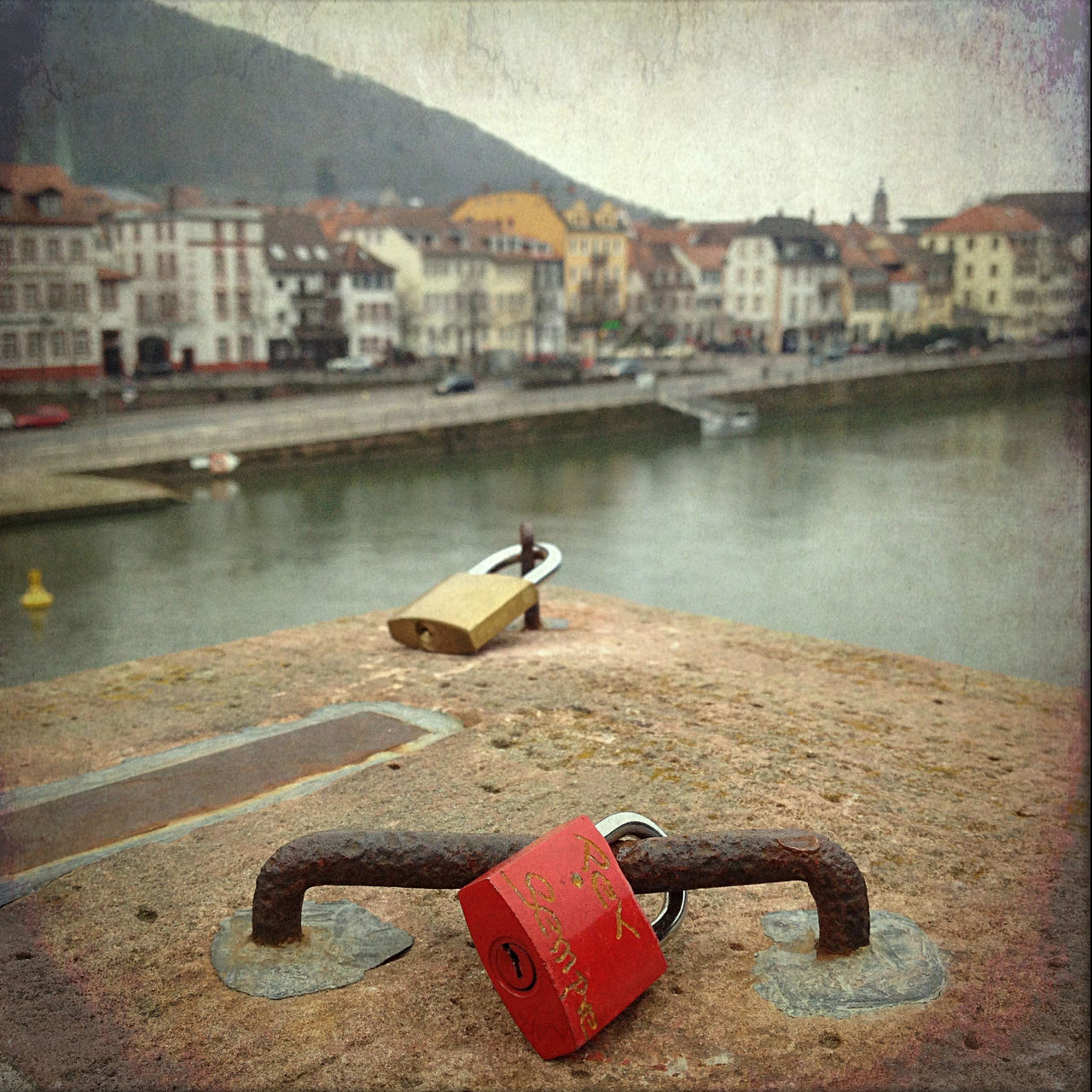 Vor der Kulisse Heidelbergs blickt man auf ein rotes Liebesschloss, das auf einem Eisen eines Brückenpfeilers verschlossen ist.