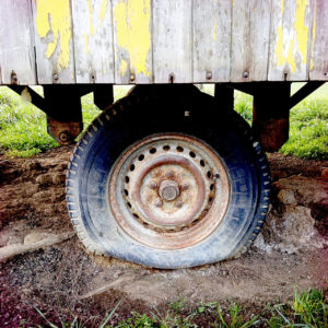 In der Bildmitte steht ein platter Reifen eines Bauwagens im Schlamm. Der Aufbau nimmt das obere Drittel des Bilds ein