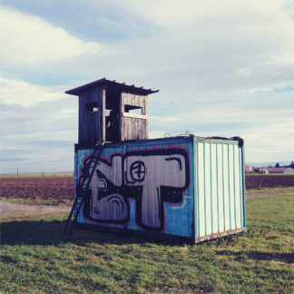 Auf einem mit Graffiti bemalten Container thront ein hölzerner Jagshochsitz.
