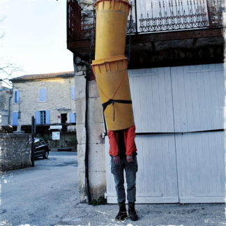 In der Röhre eines vielgliedrigen Bauschuttabfallrohres steht bis zu den Schultern sichtbar ein Mensch mit orangener Jacke und grauer Hose vor einer Hausbaustelle.