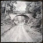 Fluchtperspektive entlang einer schnurgeraden ehemaligen Bahnstrecke auf eine Überführung hinzu. Schwarz-weiß-Bild.
