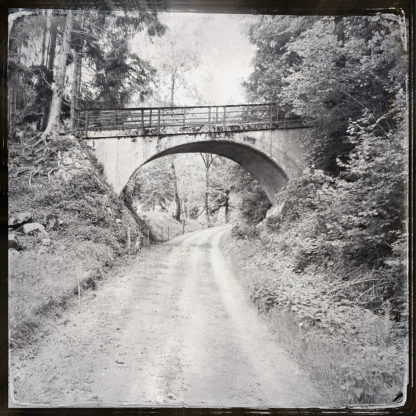 Fluchtperspektive entlang einer schnurgeraden ehemaligen Bahnstrecke auf eine Überführung hinzu. Schwarz-weiß-Bild.