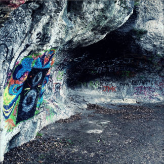 Eine kleine Felsenhöhle, die über und über mit Graffitis bemalt ist.