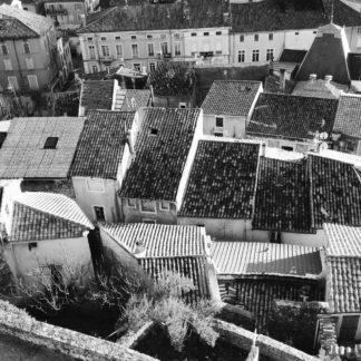 Von einer Burgmauer schaut man auf die Dächer einer dicht bebauten, verwinkelten Stadt. Schwarz-weiß-Aufnahme.