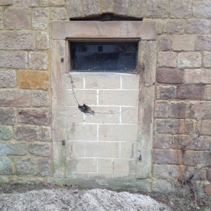 Mit Bimssteinen vermauerte Tür in einer Wand aus beige-rotem Sandstein.