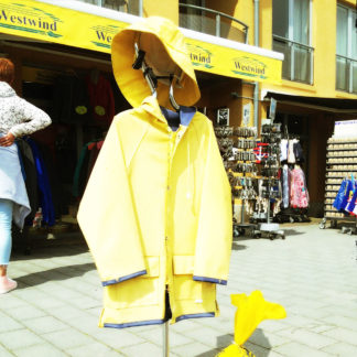 Ein gelber Regenmantel auf einem Kleiderständer vor einer touristischen Verkaufszeile in einer norddeuteschen Stadt.