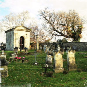 Zwei Gräber vorne und eine große Gruft vor Friedhofsmauer und kahlen Bäumen