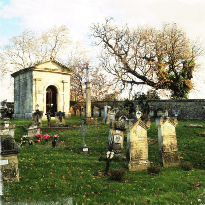 Zwei Gräber vorne und eine große Gruft vor Friedhofsmauer und kahlen Bäumen
