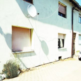 Schattenwurf einer Satellitenschüssel an weißer Hauswand eines Wohngebäudes.