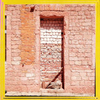 Mit Kalksteinen vermauerte Tür in einer roten Sandsteinwand. Schräg steht ein Stock im Gewände