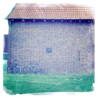 Flächiges Bild mit blassem Grün unten, violett-grauer Wand darüber und blassem Ziegeldach ganz oben. An der Wand lehnen unscheinbar zwei Fahrräder
