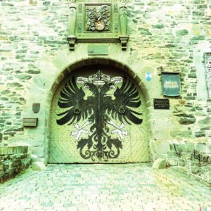 Ein grünlich verfärbtes, zartblasses Portal mit Rundbogen und großem Wappen auf den beiden Flügeln des Tores. Ein stilisierter Adler.