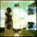 Gespiegelte Szene einer Denkmalsbüste neben dänischer Flagge.