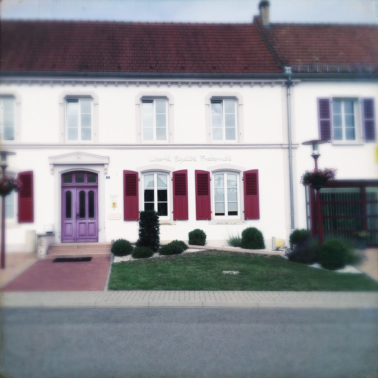 Haus an einer Dorfdurchgangsstraße. Rote Fensterläden, Steingarten, Tür