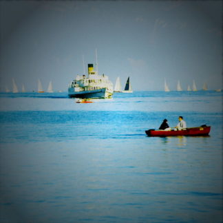 Fehlfarbenbild mit übersättigtem Blau. Rotes Ruderboot am rechten Bildrand, mittig vor Fährschiff am Horizont etwas nach links gerückt und im oberen Bilddrittel.