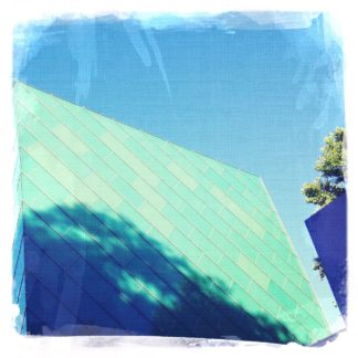 Blaue Hausfassade mit Schatten eines Baumes unter Himmel. Das Bild besteht aus verschiedenen bläulich gefärbten Flächen