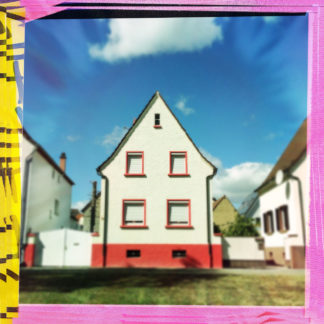 Kleines Haus frontal gesehen mit knallrotem Sockel. Das Bild hat einen bunten rosa-gelben Rahmen. Je zwei nebeneinanderliegende Fenster in den beiden Stockwerken und eine kleine Luke mittig im Giebel. Blauer Himmel mit fetter weißer Wolke.