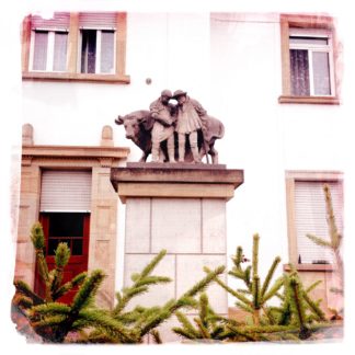 Ein bäuerliches Denkmal auf einem dicken Sockel in einem Vorgarten eines vorstädtischen Wohnhauses zeigt einen Mann, der einen Bullen führt.