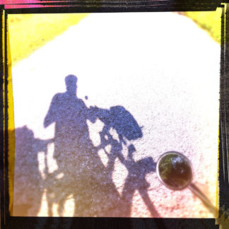 Schatten eines Fahrradfahrers oder einer Fahrradfahrerin mit Helm auf fast bleichem Teer, Fehlbelichtung mit gelblichem Einschlag und scharzem Rand, der an der linken oberen Ecke ins rötliche driftet. Neben dem Schatten ragt von rechts ein kleiner runder Fahrradspiegel ins Bild.