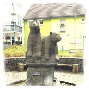 Zwei kleine Bärenfiguren aus Stein in einem leeren, außerbetrieben Springbrunnen.