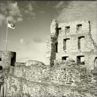 Schwarzweißbild einer Burgmauer. Auf dem runden Turm links im Bild weht eine Fahne