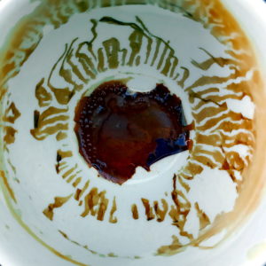Ziemlich abstrakte runde Struktur, aus der man gewillt sein mag, Schriftzeichen im fernöstlichen oder israelischen Stil zu lesen. Das dunkle Zentrum gibt endlich Aufschluss, dass es sich bei der Szene um den Blick in eine leergetrunkene Kaffeetasse handelt.