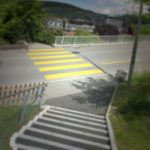 Treppab mündet der Fußweg auf einer Straße und wird dem Rhythmus der Treppe genüge tragend von einem gelben Zebrastreifen fortgesetzt bis zur Kante der Hangstraße. Im Hintergrund ahnt man die Stadt. Vignette vernebelt die Szene und verleiht ihr einen mystisch-verträumten Hauch.